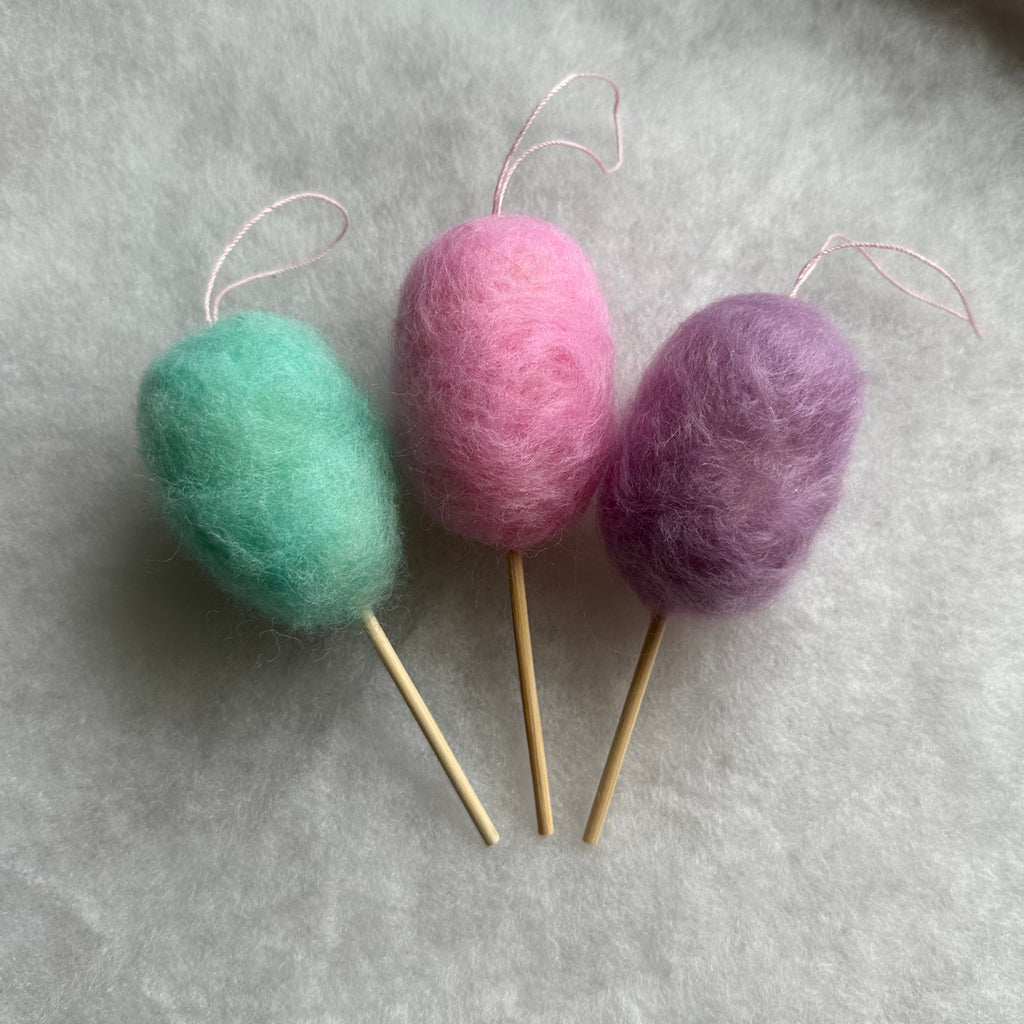 Three colorful felted cotton candy ornaments against a gray background