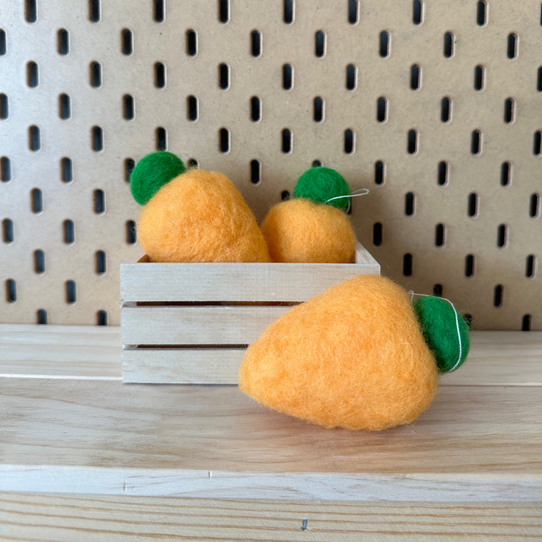 Felted carrot ornaments in a wooden crate.