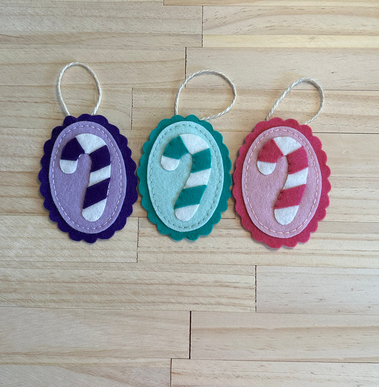 Trio of candy cane motif wool felt ornaments in purple, blue and pink.